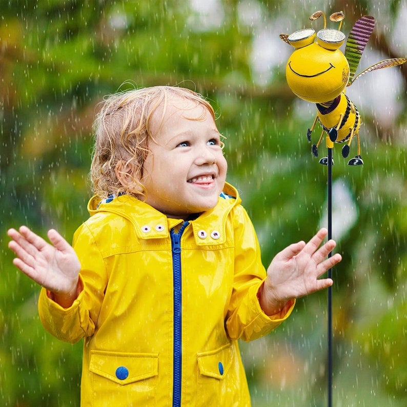 May include: A yellow metal bee garden stake with black and white details. The bee has large, round eyes and a smiling face. The bee is attached to a black metal stake. May include: A yellow metal bee garden stake with black and white details. The bee has large, round eyes and a smiling face. The bee is attached to a black metal stake.