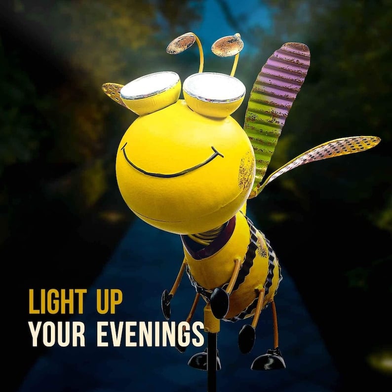 May include: A yellow metal bee with a smiling face and black and yellow stripes. The bee has two large white lights on its head. The bee is standing on a metal stake. The text 'LIGHT UP YOUR EVENINGS' is in the lower left corner of the image. May include: A yellow metal bee with a smiling face and black and yellow stripes. The bee has two large white lights on its head. The bee is standing on a metal stake. The text 'LIGHT UP YOUR EVENINGS' is in the lower left corner of the image.